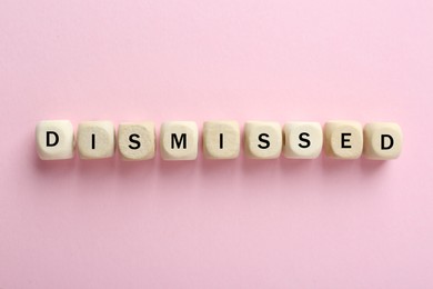 Image of Word Dismissed made of wooden cubes on pink background, top view
