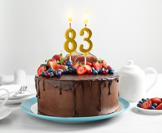 Image of Yummy chocolate cake with fruits and burning number shaped candles on white table. 83th birthday or other special occasion