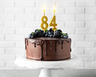 Image of Yummy chocolate cake with berries and burning number shaped candles on table. 84th birthday or other special occasion