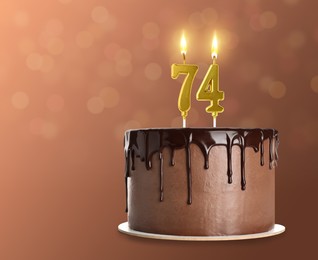 Image of Yummy chocolate cake with burning number shaped candles on brown background, space for text. 74th birthday or other special occasion
