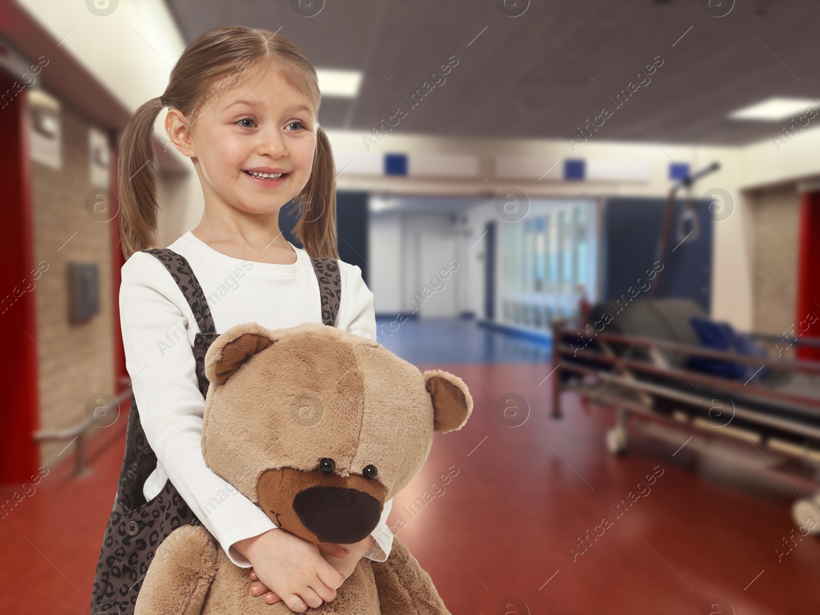 Image of Cute little girl with toy bear in hallway of children's hospital