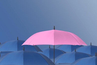 Image of Pink umbrella among blue ones against color background