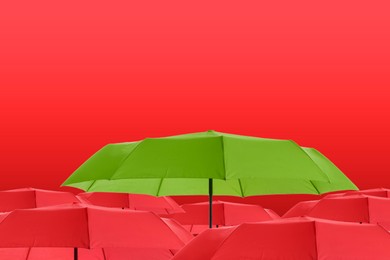 Image of Green umbrella among red ones against color background
