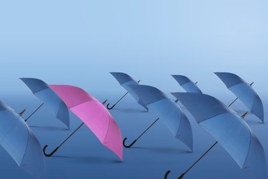 Image of Pink umbrella among blue ones against color gradient background