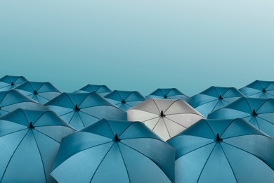 Image of White umbrella among blue ones against color background