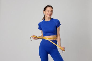 Photo of Beautiful woman measuring her belly with tape on gray background
