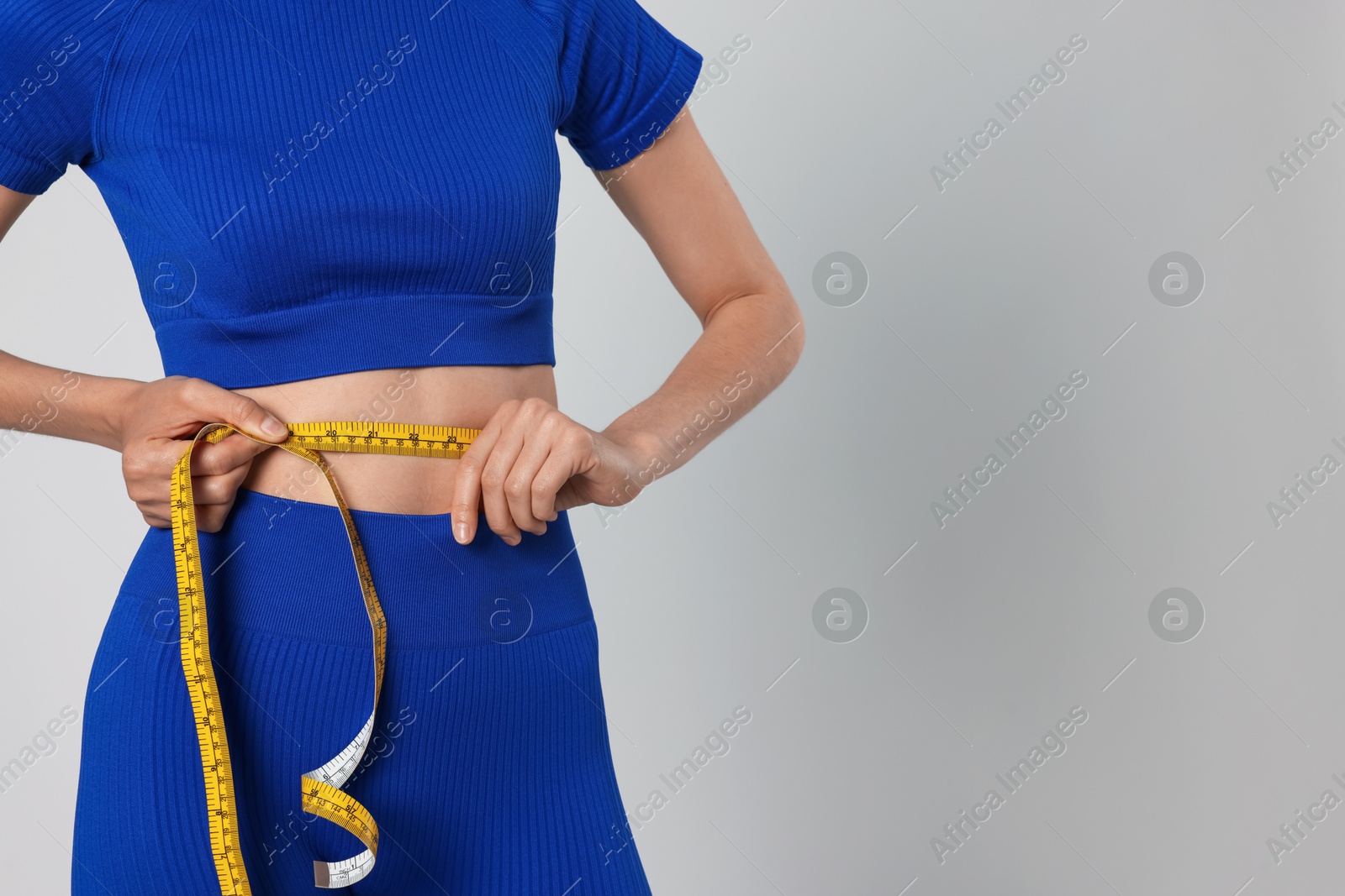 Woman measuring her belly with tape on gray background, closeup. Space for text Photo of Woman measuring her belly with tape on gray background, closeup. Space for text