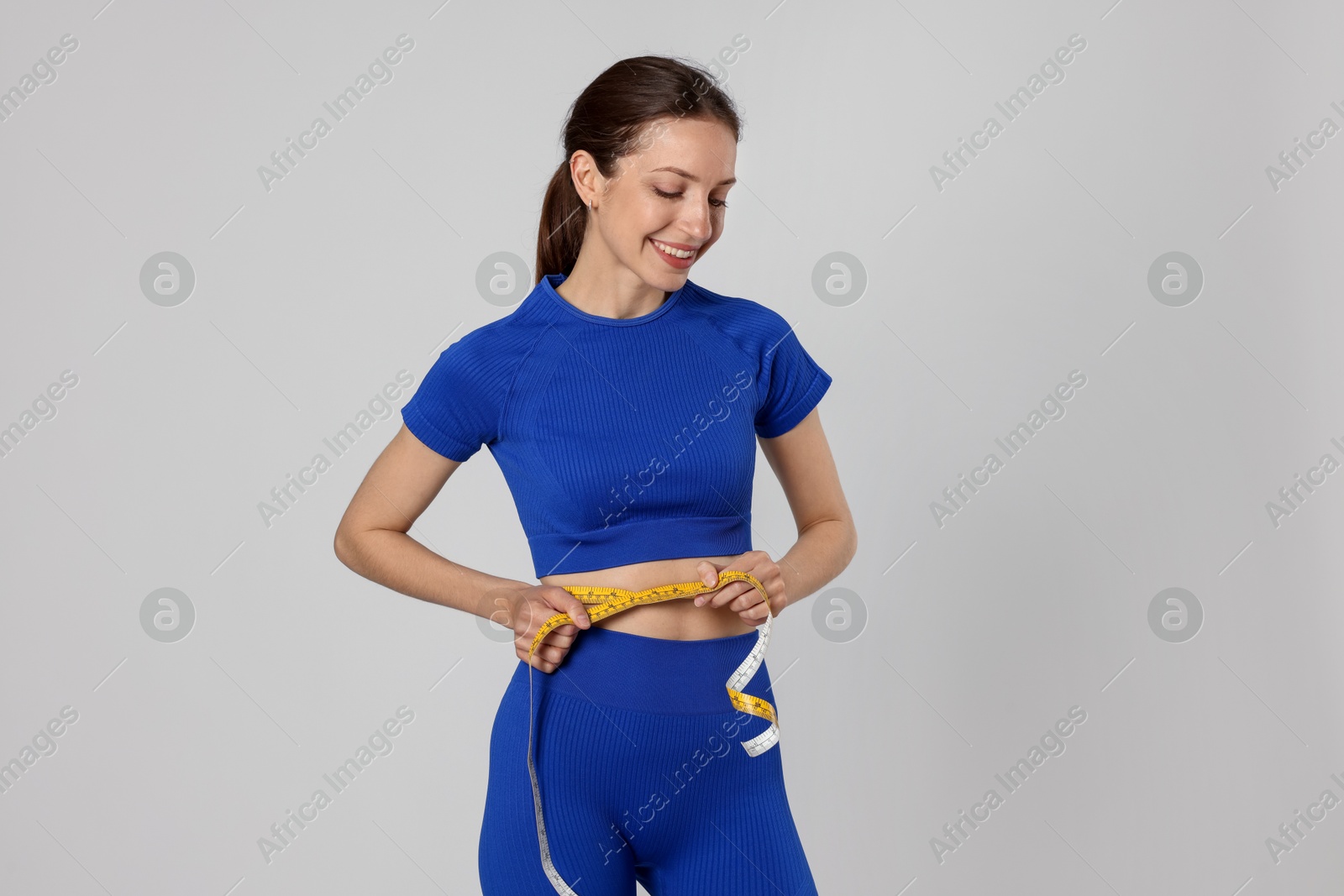 Beautiful woman measuring her belly with tape on gray background Photo of Beautiful woman measuring her belly with tape on gray background