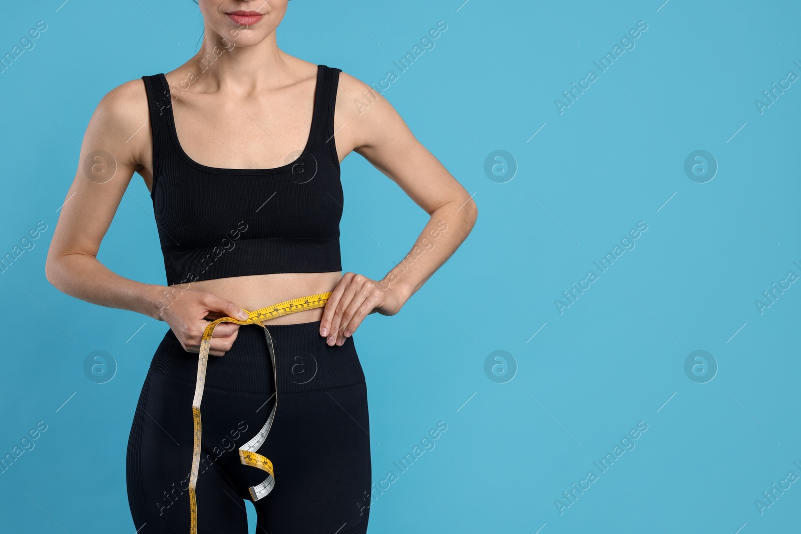 Woman measuring her belly with tape on light blue background, closeup. Space for text Photo of Woman measuring her belly with tape on light blue background, closeup. Space for text