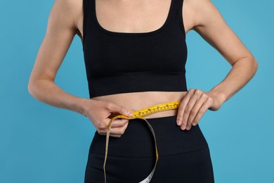 Photo of Woman measuring her belly with tape on light blue background, closeup