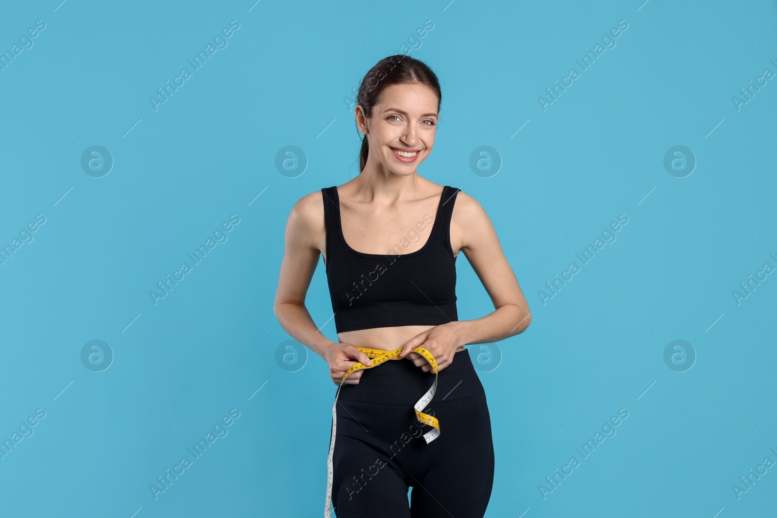 Beautiful woman measuring her belly with tape on light blue background Photo of Beautiful woman measuring her belly with tape on light blue background