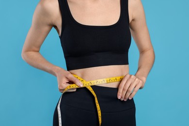 Photo of Woman measuring her belly with tape on light blue background, closeup