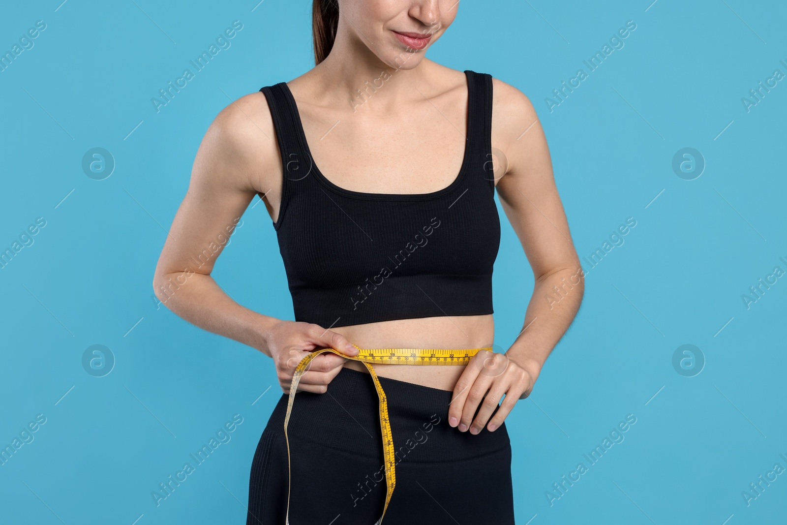 Photo of Woman measuring her belly with tape on light blue background, closeup