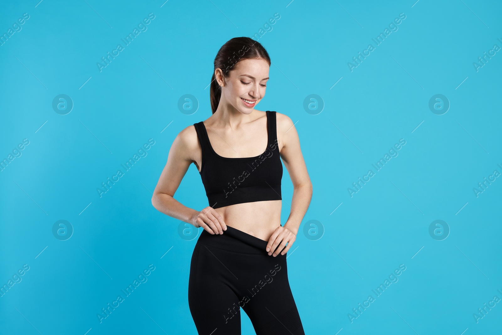 Beautiful woman with flat belly on light blue background Photo of Beautiful woman with flat belly on light blue background