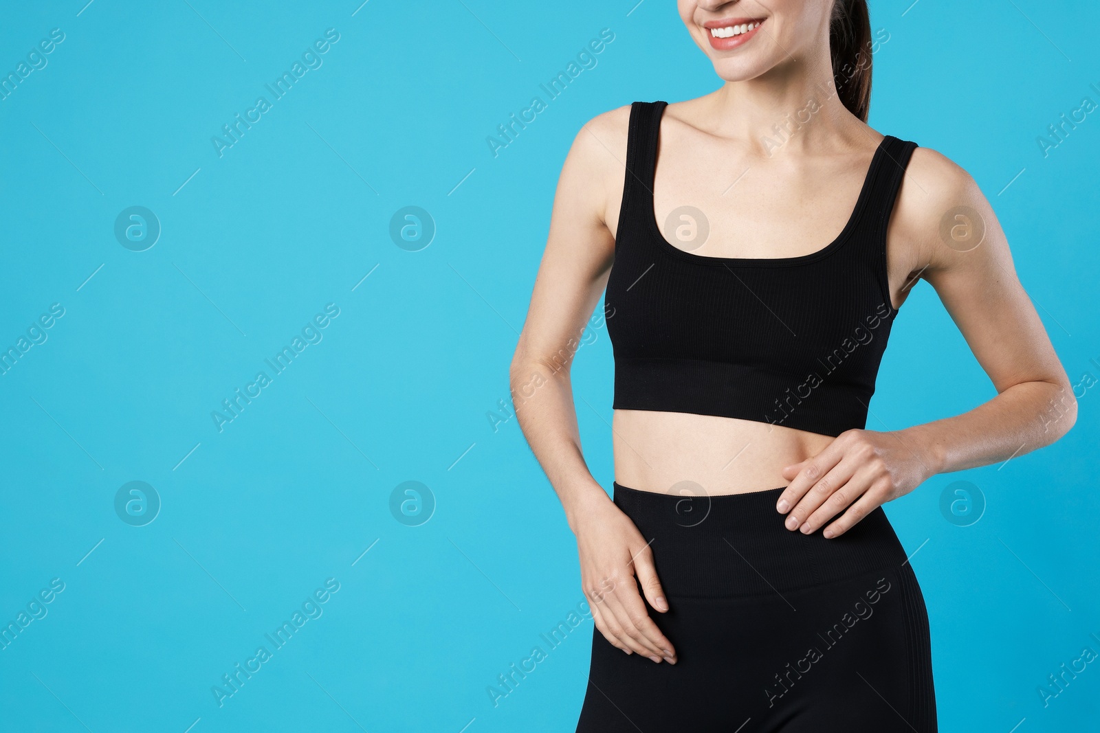 Beautiful woman with flat belly on light blue background, closeup. Space for text Photo of Beautiful woman with flat belly on light blue background, closeup. Space for text