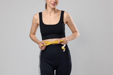 Photo of Woman measuring her belly with tape on gray background, closeup
