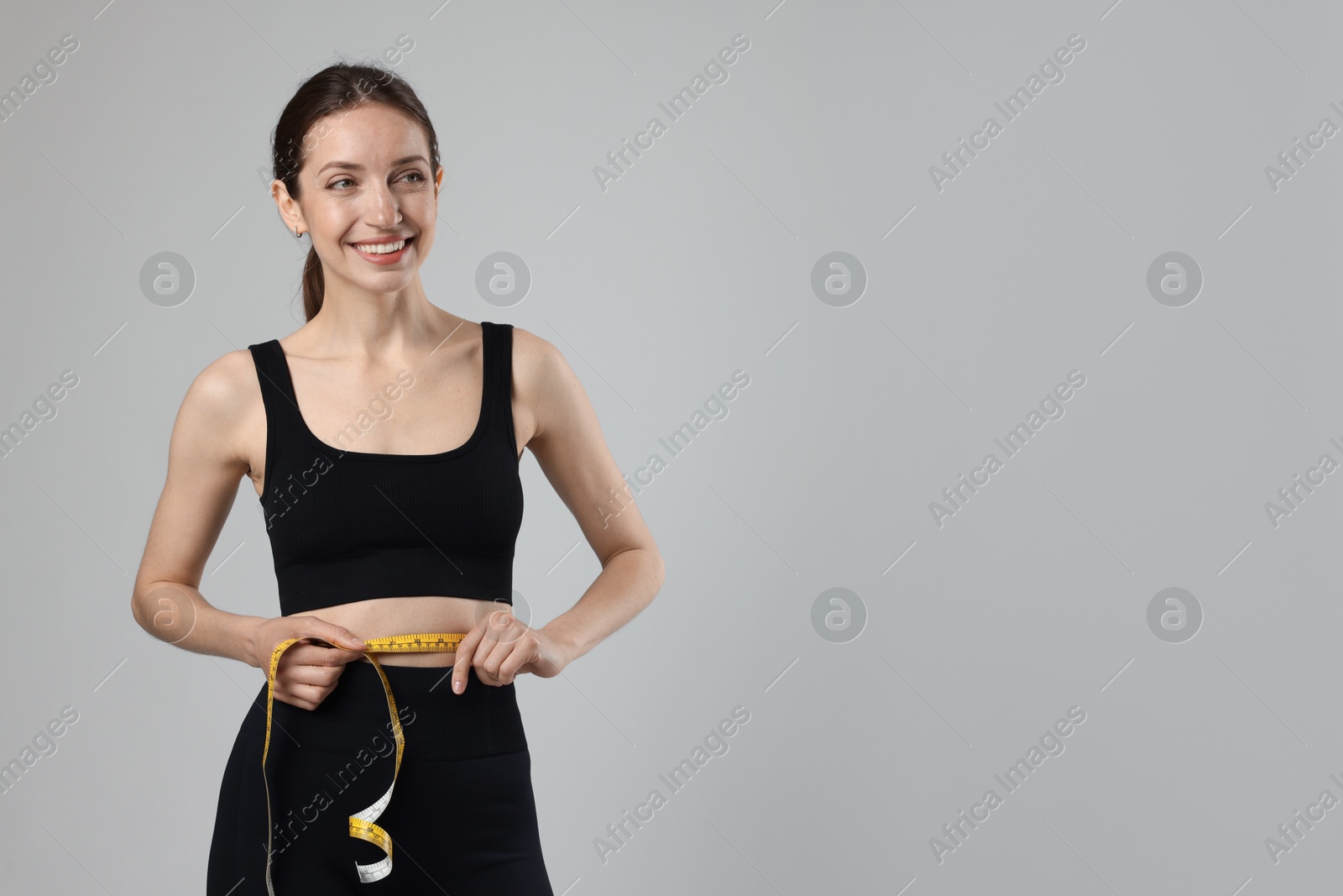 Beautiful woman measuring her belly with tape on gray background, space for text Photo of Beautiful woman measuring her belly with tape on gray background, space for text
