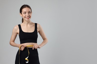 Photo of Beautiful woman measuring her belly with tape on gray background, space for text