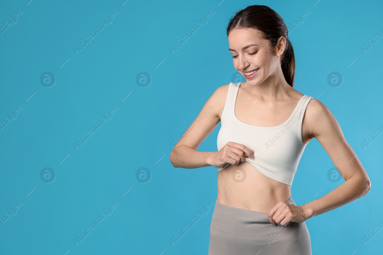 Beautiful woman with flat belly on light blue background, space for text Photo of Beautiful woman with flat belly on light blue background, space for text