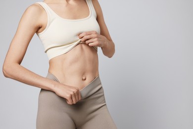 Photo of Beautiful woman with flat belly on gray background, closeup. Space for text