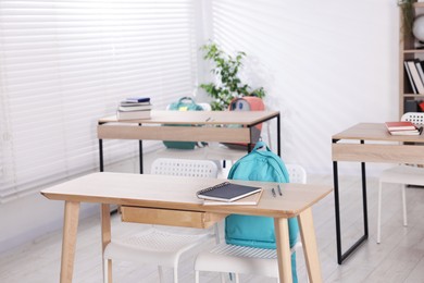 Photo of Empty classroom with wooden desks, chairs and backpacks