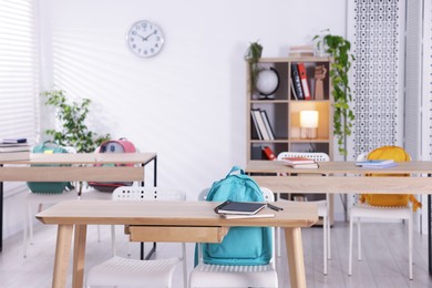 Photo of Empty classroom with wooden desks, chairs and backpacks