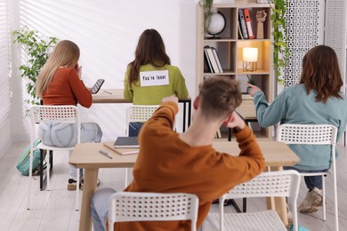 Photo of Schoolmates bullying teenage girl with sign You Loser on her back at school