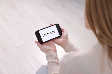 Photo of Cyber bullying. Upset teenage girl looking at smartphone with text You Loser at home, closeup
