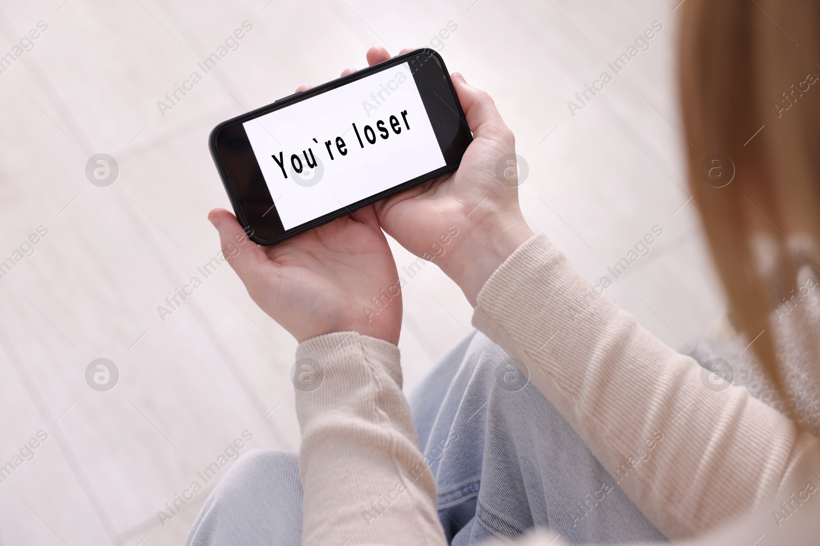 Cyber bullying. Upset teenage girl looking at smartphone with text You Loser at home, closeup Photo of Cyber bullying. Upset teenage girl looking at smartphone with text You Loser at home, closeup