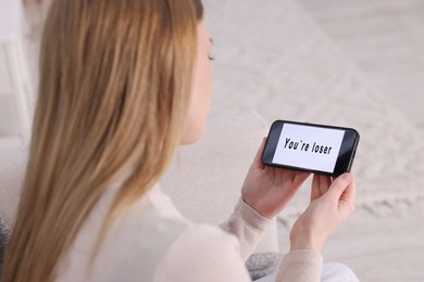 Photo of Cyber bullying. Upset teenage girl looking at smartphone with text You Loser at home, closeup