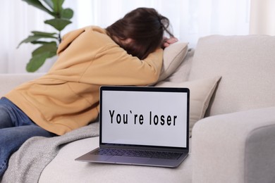 Photo of Cyber bullying. Upset teenage girl and laptop with text You Loser on sofa at home, selective focus