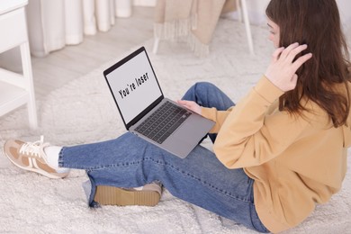 Photo of Cyber bullying. Upset teenage girl and laptop with text You Loser on floor indoors