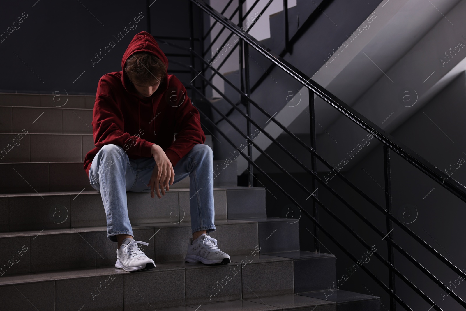 Bullying. Upset teenage boy on stairs indoors. Space for text Photo of Bullying. Upset teenage boy on stairs indoors. Space for text
