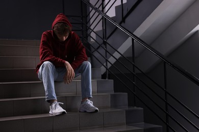 Photo of Bullying. Upset teenage boy on stairs indoors. Space for text