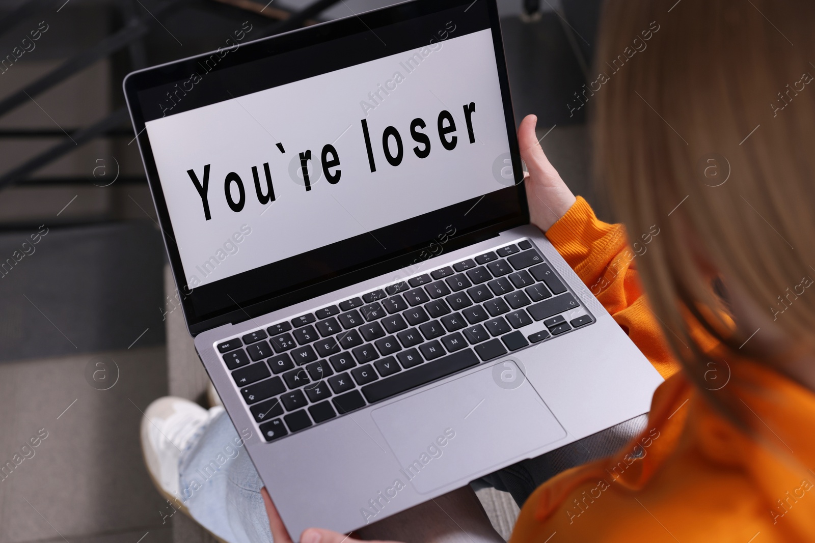 Cyber bullying. Upset teenage girl looking at laptop with text You Loser on stairs indoors, closeup Photo of Cyber bullying. Upset teenage girl looking at laptop with text You Loser on stairs indoors, closeup