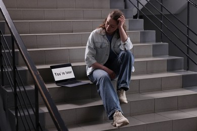 Photo of Cyber bullying. Upset teenage girl and laptop with text You Loser on stairs indoors