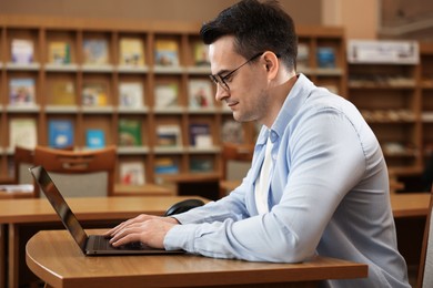 Photo of Man working on laptop at desk in public library