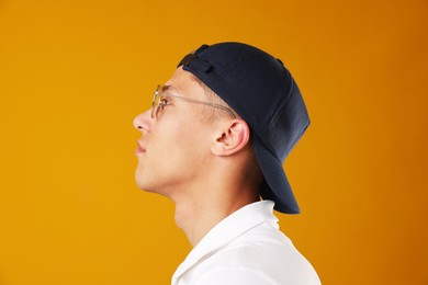 Photo of Young man in stylish baseball hat on orange background