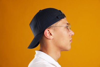 Photo of Young man in stylish baseball hat on orange background