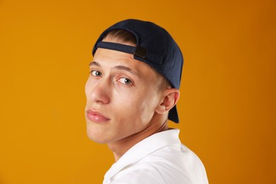 Photo of Young man in stylish baseball hat on orange background
