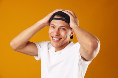 Photo of Young man in stylish baseball hat on orange background