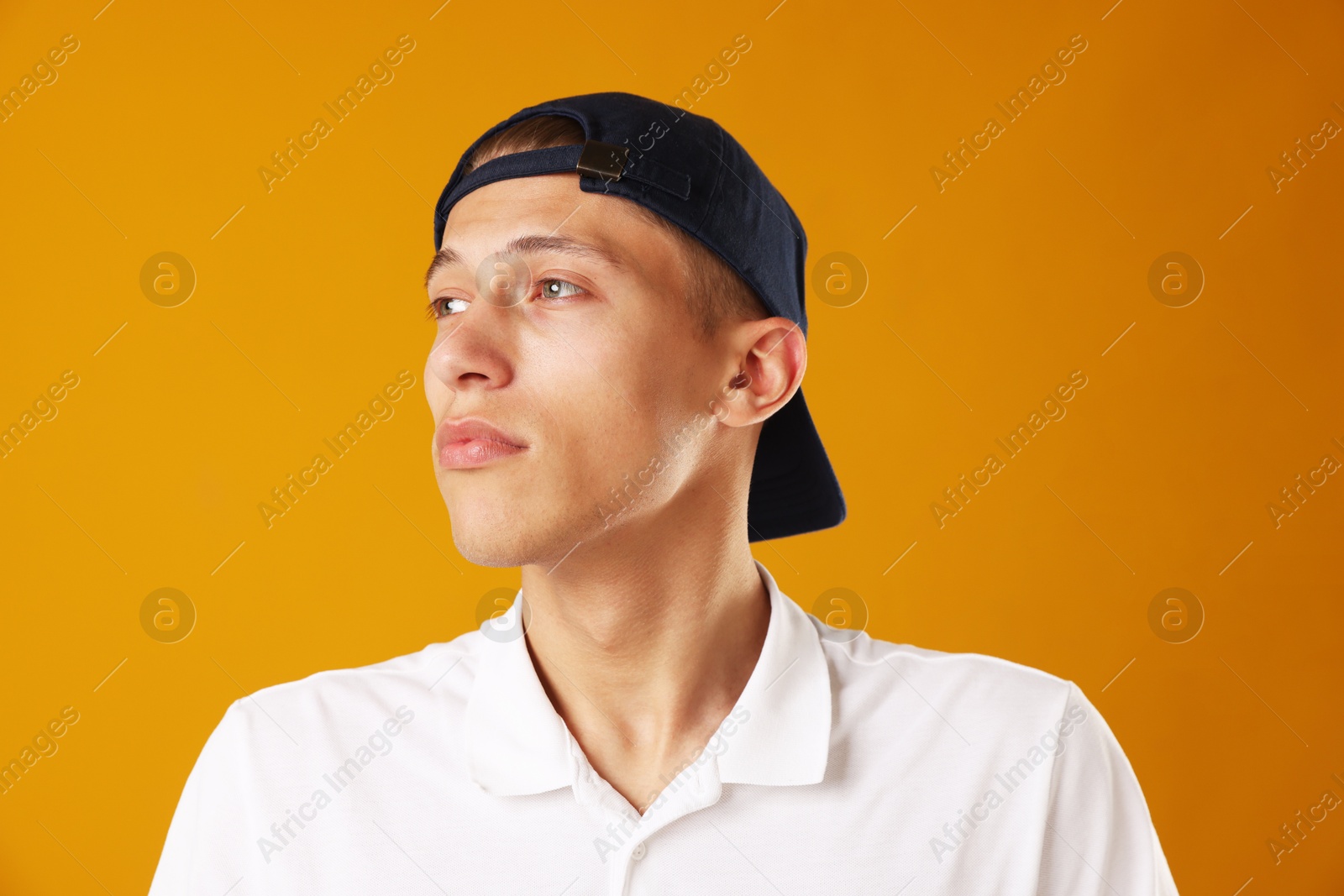 Young man in stylish baseball hat on orange background Photo of Young man in stylish baseball hat on orange background