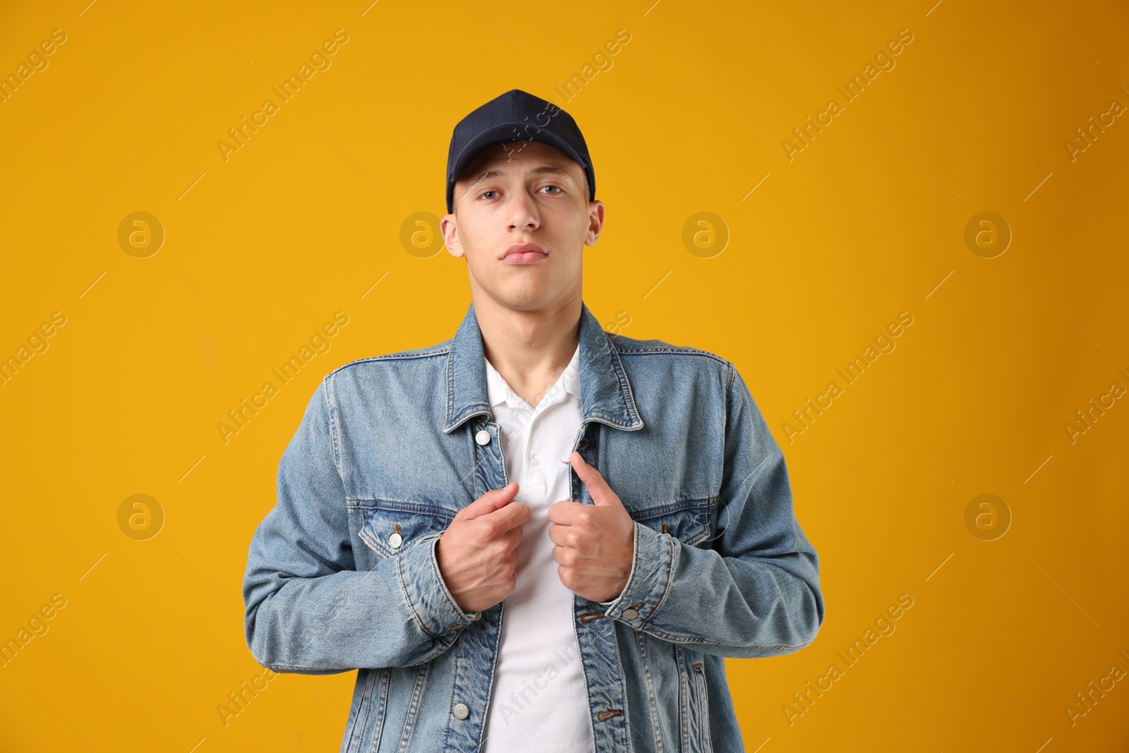 Young man in stylish baseball hat on orange background Photo of Young man in stylish baseball hat on orange background