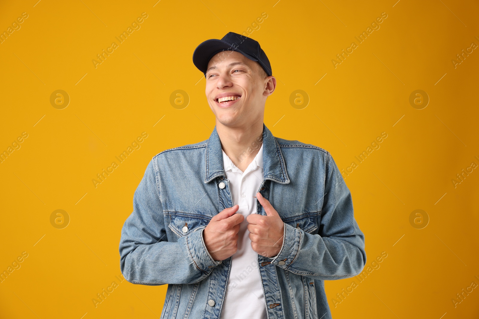Young man in stylish baseball hat on orange background Photo of Young man in stylish baseball hat on orange background