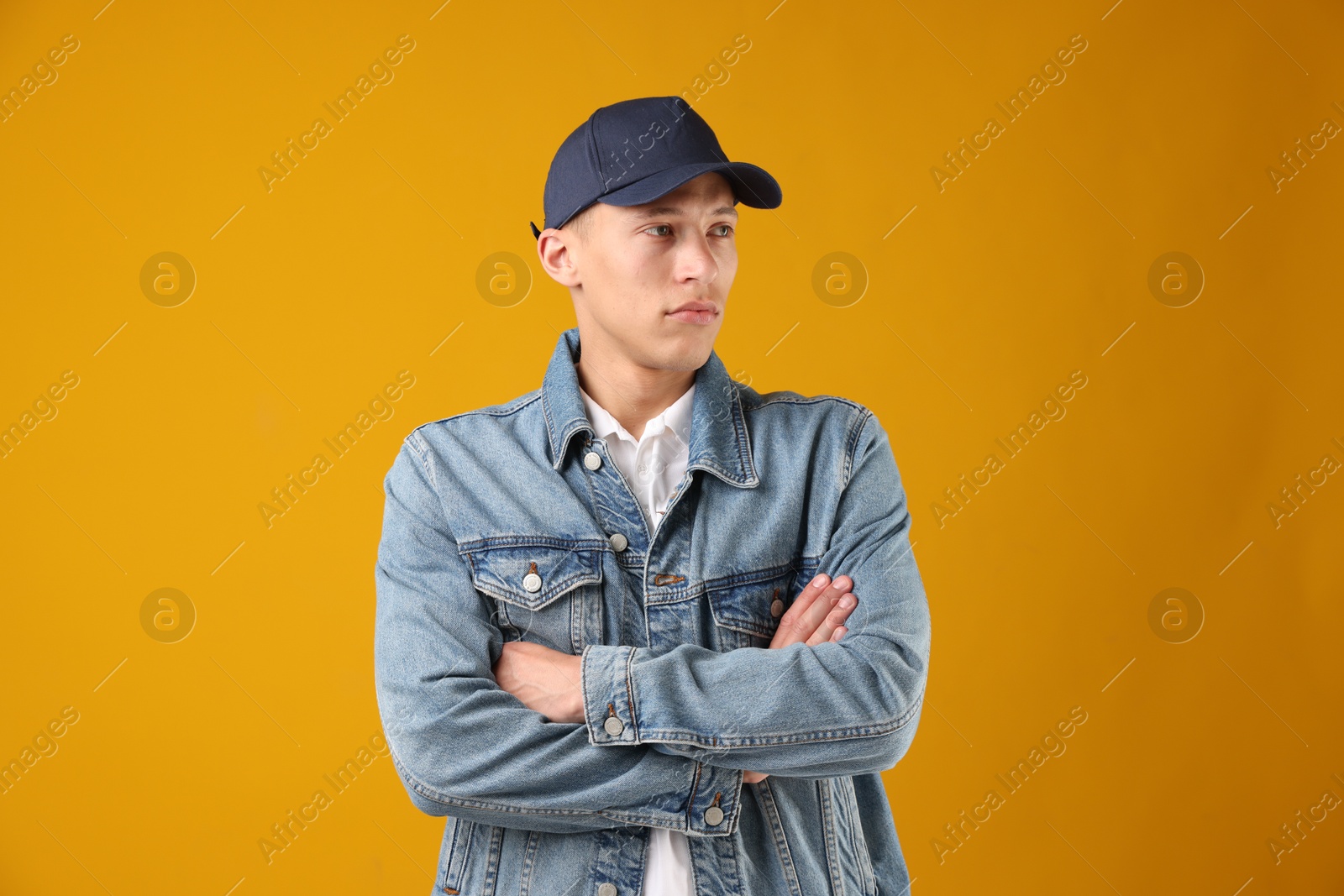 Young man in stylish baseball hat on orange background Photo of Young man in stylish baseball hat on orange background