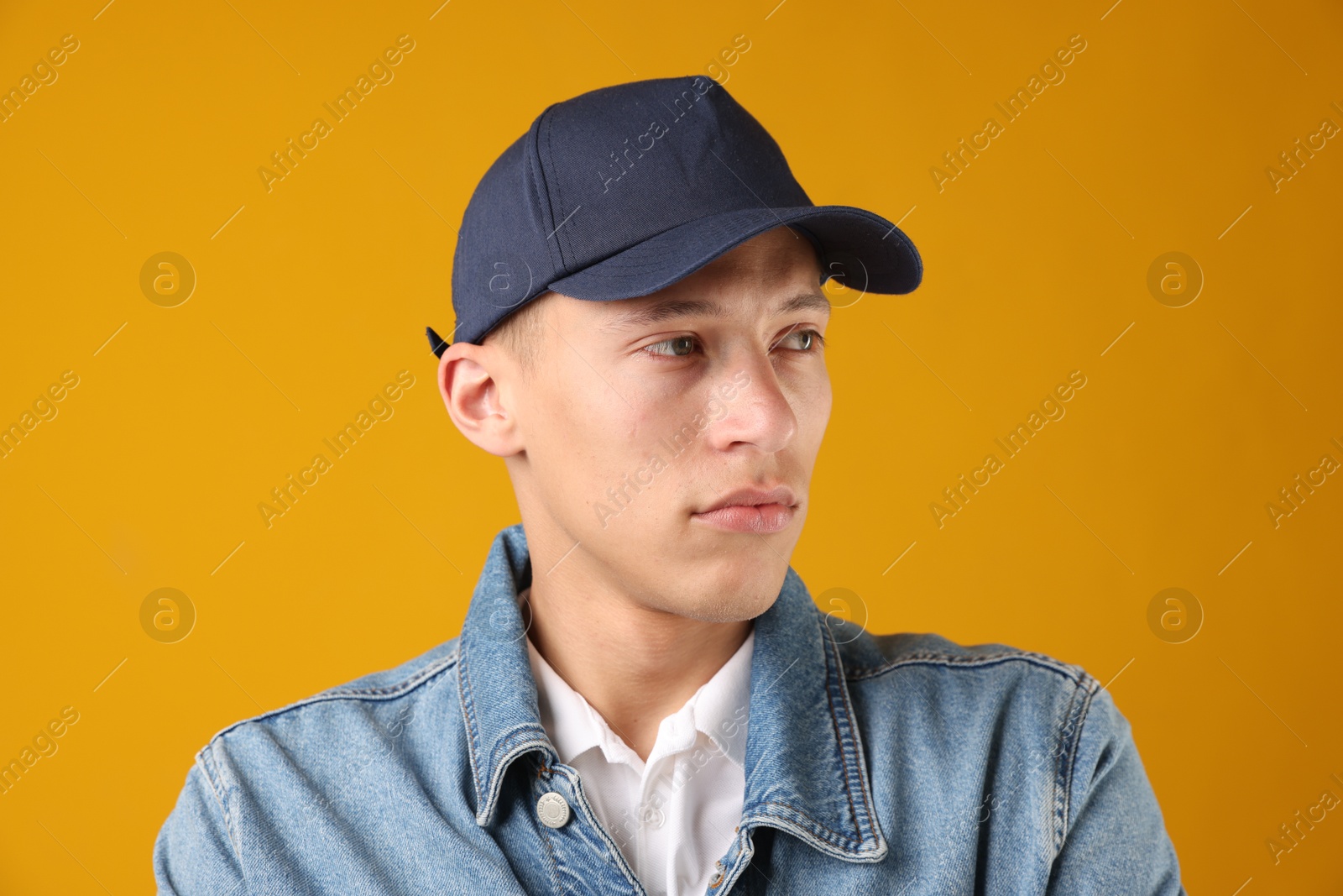 Young man in stylish baseball hat on orange background Photo of Young man in stylish baseball hat on orange background