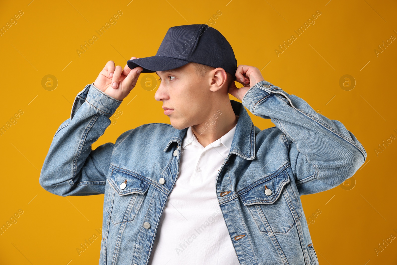 Young man in stylish baseball hat on orange background Photo of Young man in stylish baseball hat on orange background