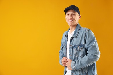 Photo of Young man in stylish baseball hat on orange background, space for text