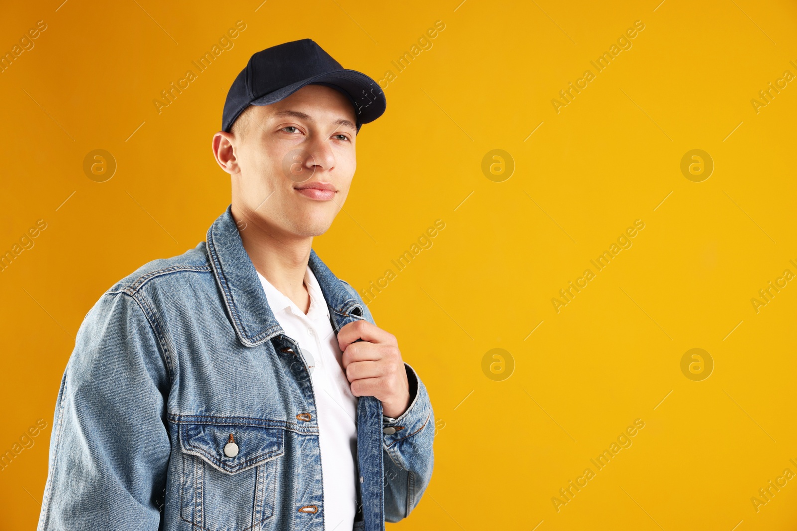 Young man in stylish baseball hat on orange background, space for text Photo of Young man in stylish baseball hat on orange background, space for text