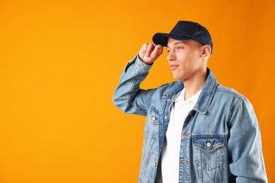 Photo of Young man in stylish baseball hat on orange background, space for text